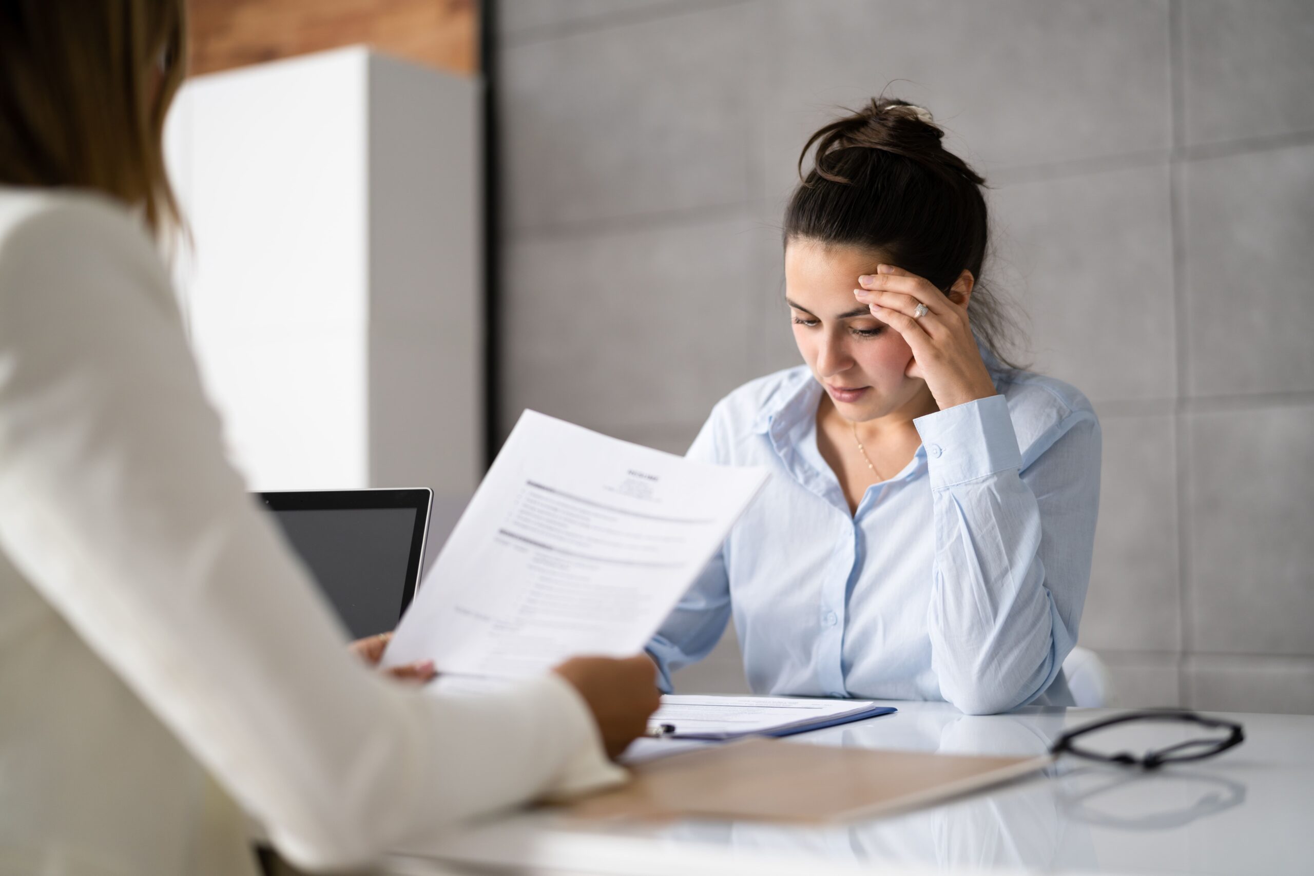 A stressed woman reviewing documents in an office meeting.